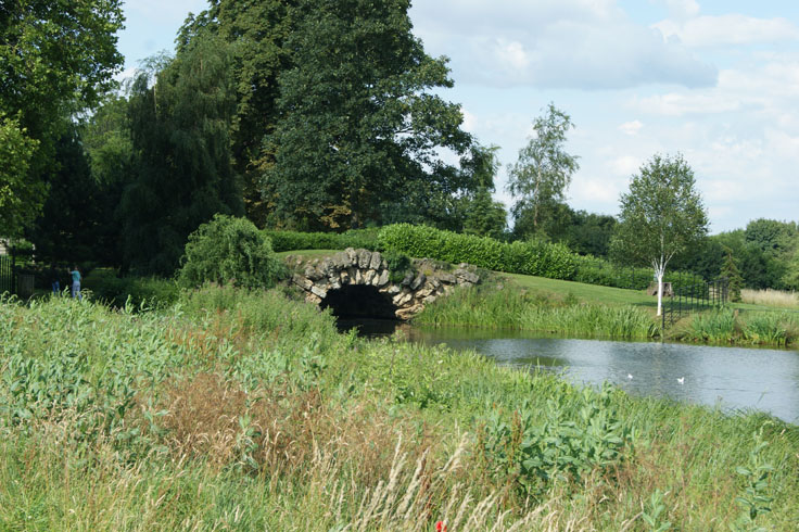 A bridge with a river flowing through it. Two children are on the left of the bridge.